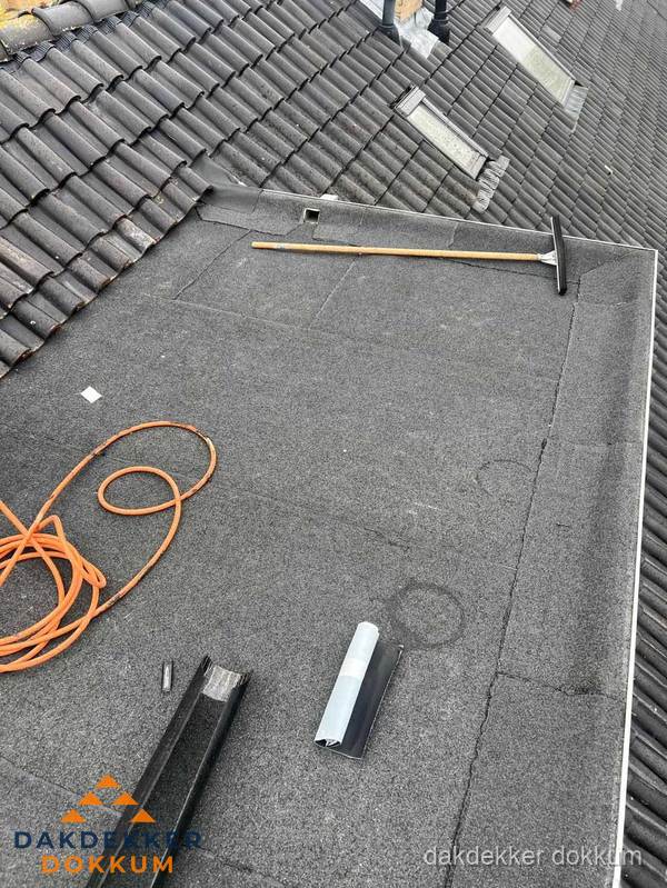 Plat dak reparatie met gereedschap en loodstroken in Dokkum