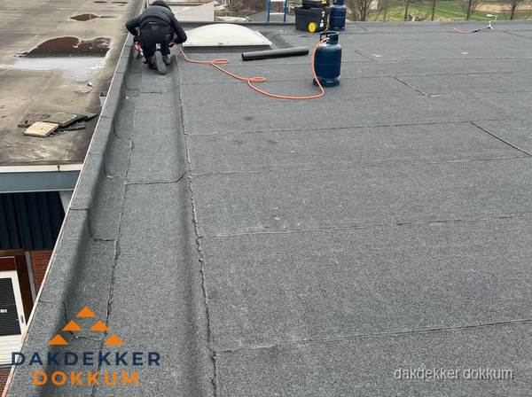 Dakdekker repareert bitumen dakbedekking op groot plat dak in Dokkum